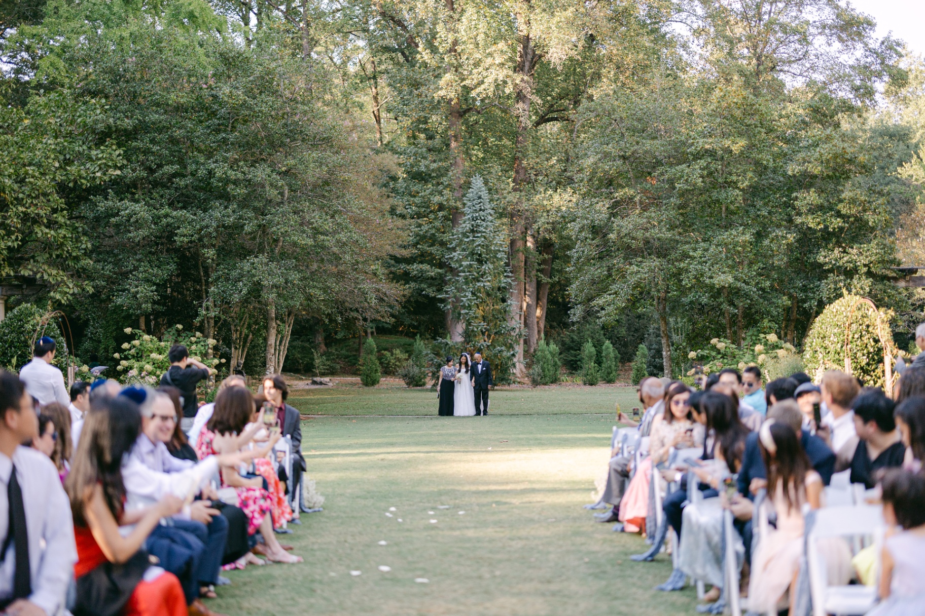 Bride being walked down a garden aisle at golden hour